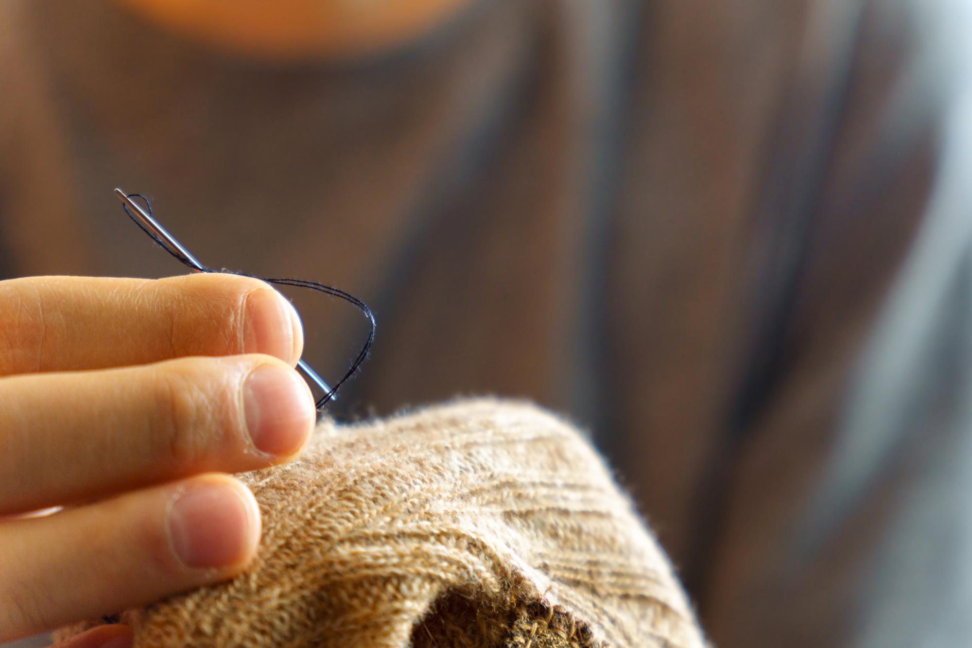 hands threading needle over linen